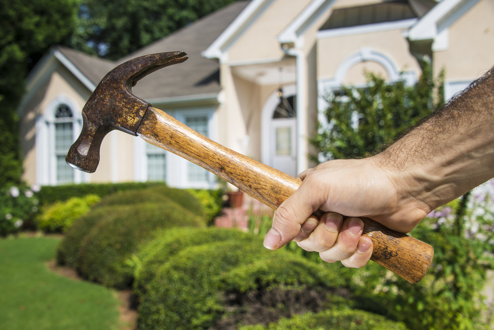 Mans hand holding hammer in front of a house indicating home improvement and maintenance. Mans hand holding hammer in front of a house indicating home improvement and maintenance.